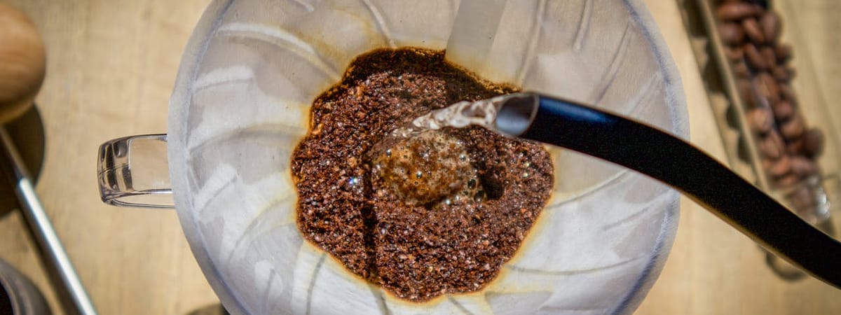 heros-img Overhead angle of pour over coffee with fresh grounds and hot water in a glass carafe.